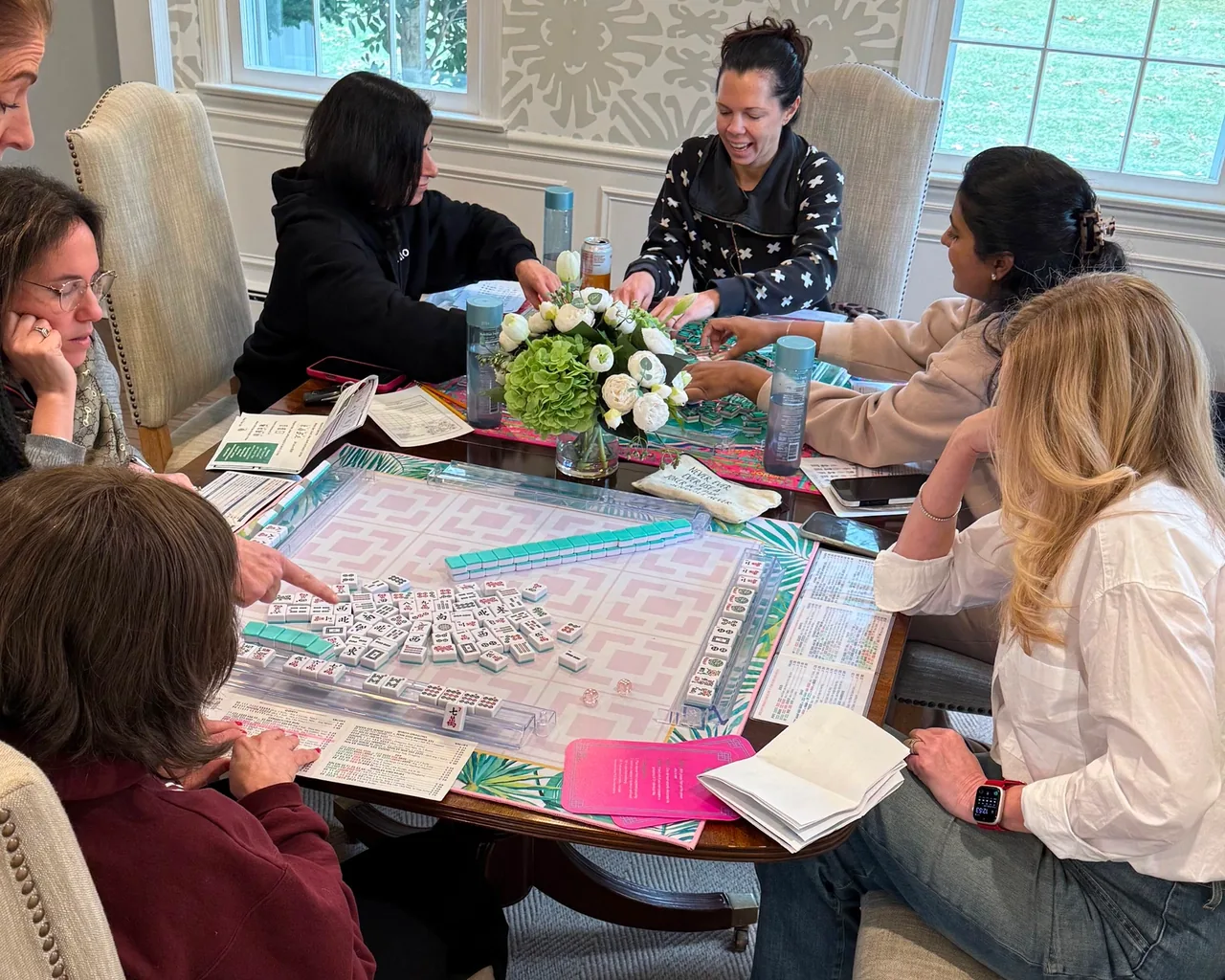 Members gathered around a Mahjong table with flowers, learning and laughing together